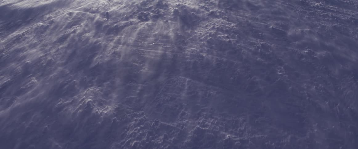 An abstract aerial shot shows wispy clouds blowing across the dark, textured surface of the ocean