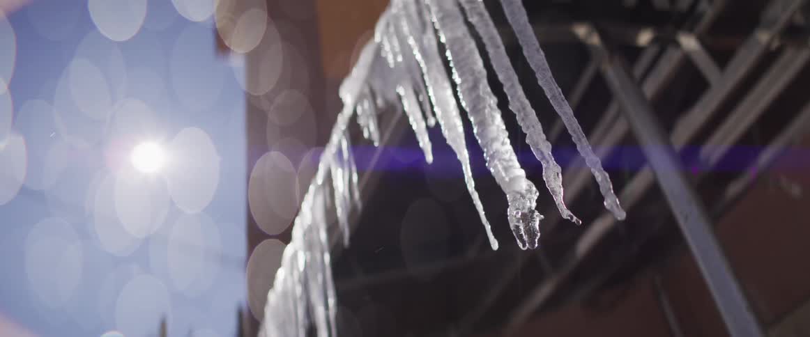 Slow motion close-up of icicles melting and dripping water in the bright sunlight, symbolizing the arrival of spring