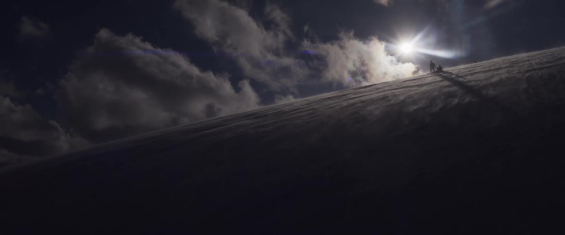 Silhouetted climbers ascend a wind-swept snowy mountain ridge as the sun flares behind them in a dramatic sky