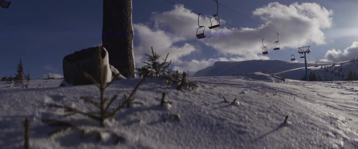 A still ski lift hangs over a pristine, snow-covered mountain under a clear blue sky with white clouds