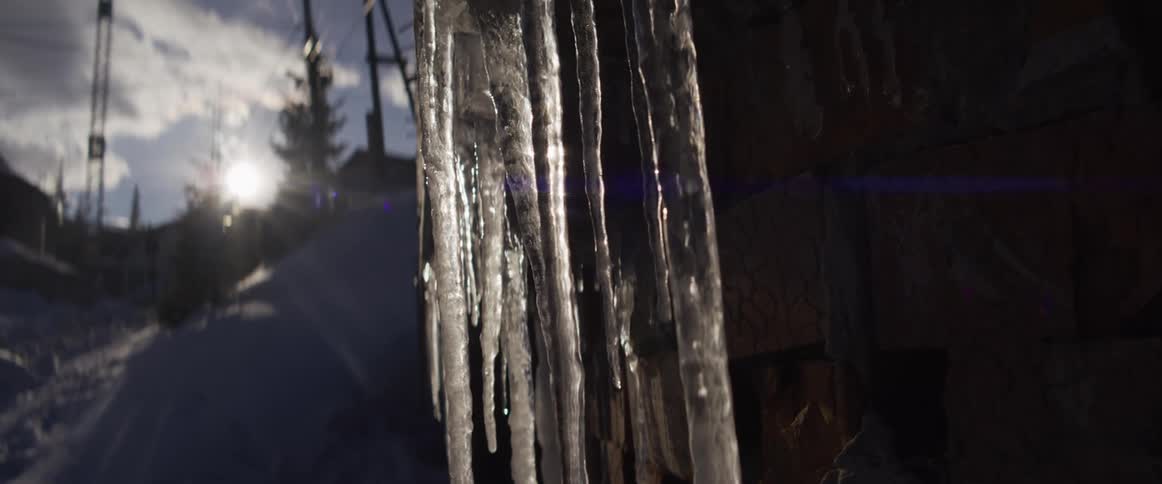 A slow motion close-up of backlit icicles hanging from a stone structure with the winter sun shining in the background