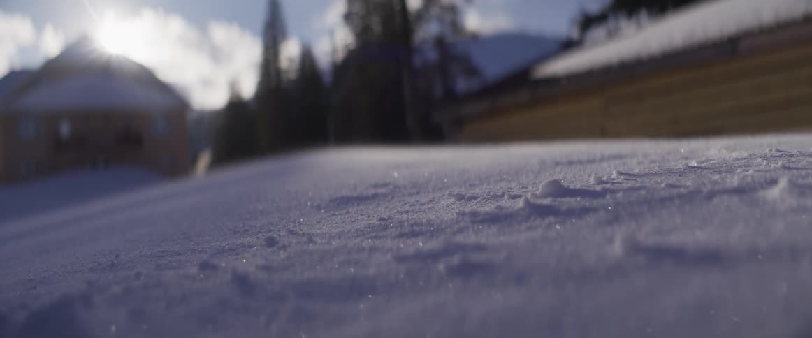 A serene, sunlit, close-up view of glittering snow being gently blown by the wind in a winter landscape