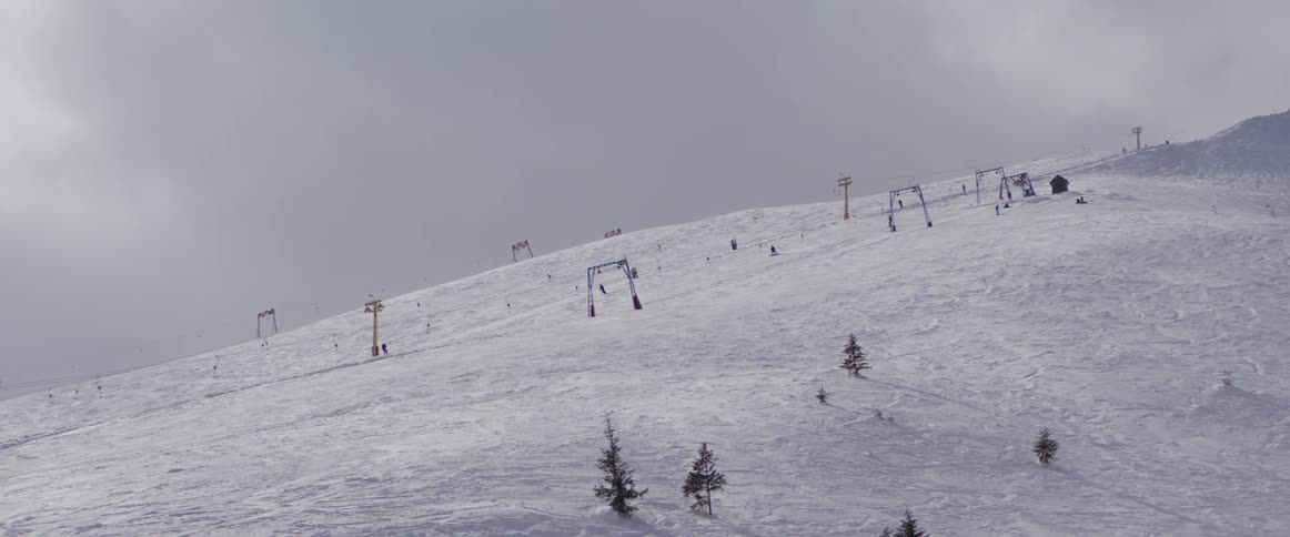 Skiers descend a snowy mountain slope next to a surface lift on an overcast winter day