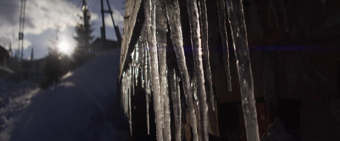 A slow-motion close-up of icicles glistening and dripping as they melt in the bright winter sun
