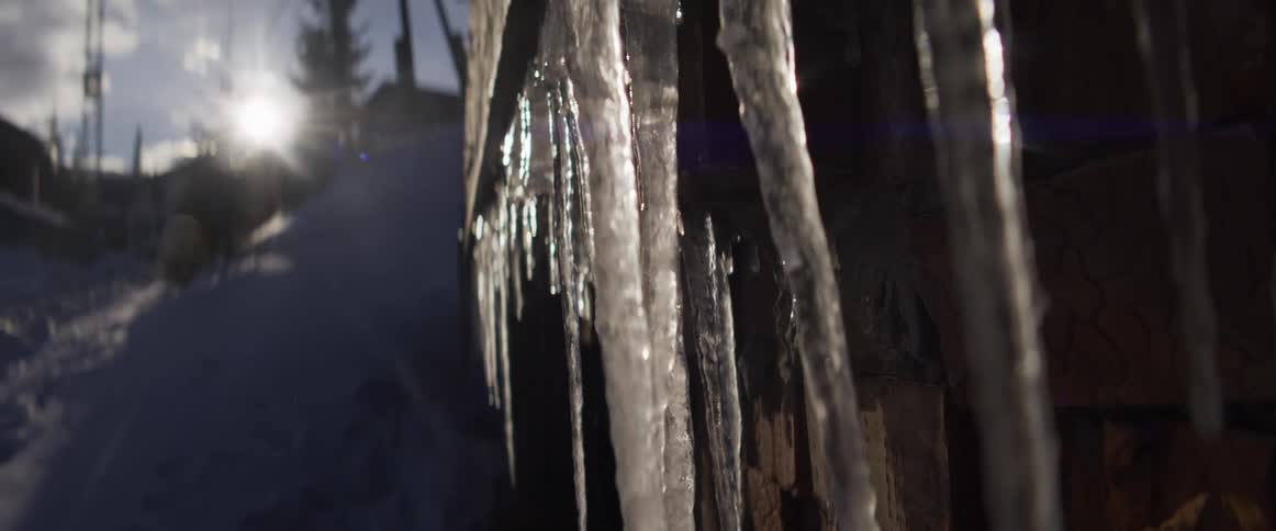 A cinematic slow-motion pan of glistening icicles hanging in a snowy environment with the bright sun flaring in the background