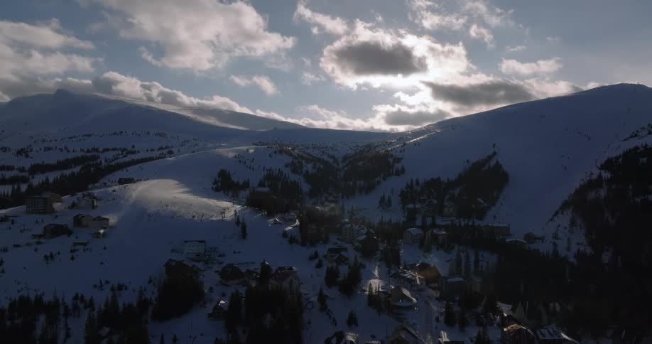 Aerial view of a quiet ski resort village nestled in a snow-covered mountain valley under a dramatic cloudy sky