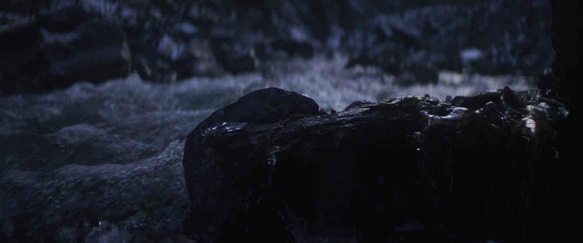 Dark and moody slow-motion close-up of a stream flowing over rocks as rain falls at night