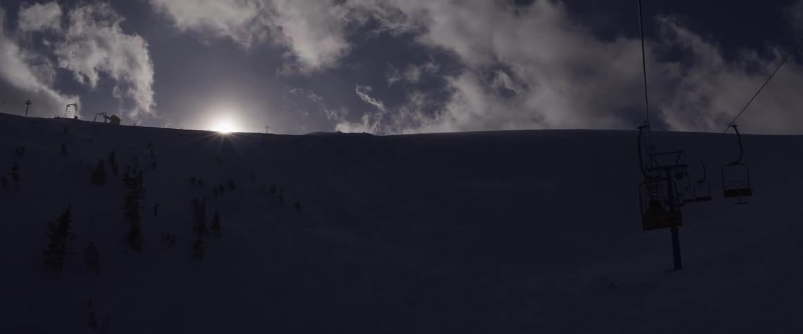 The sun crests over a vast, snow-covered mountain ridge at a ski resort