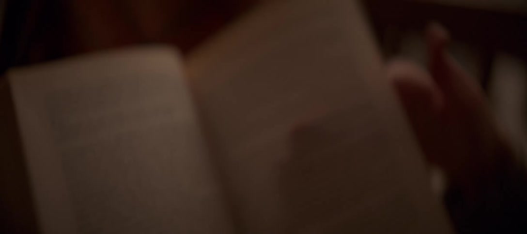 A close-up shot focuses on the text of a book as a reader turns the pages in a warm, cozy setting