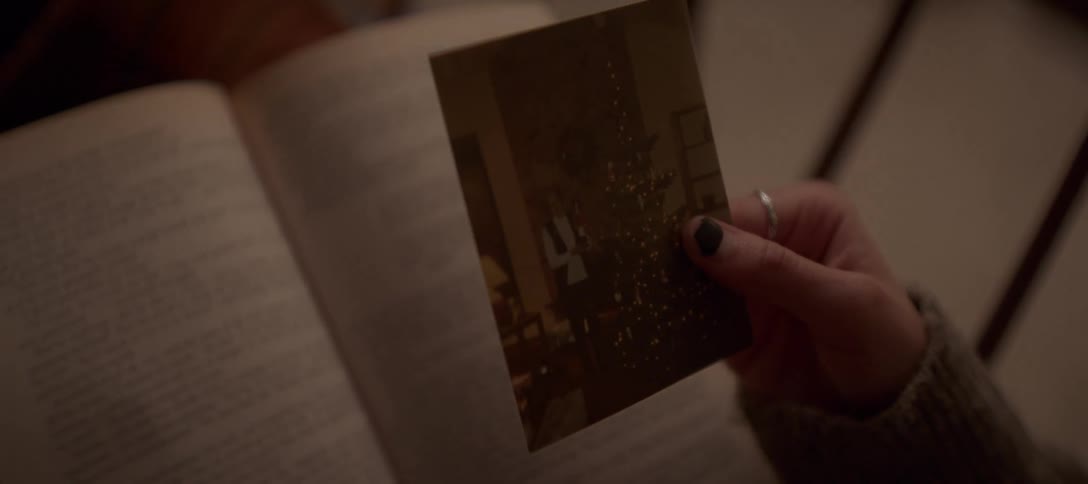 A woman's hand holds a nostalgic old photograph of a child by a Christmas tree over an open book