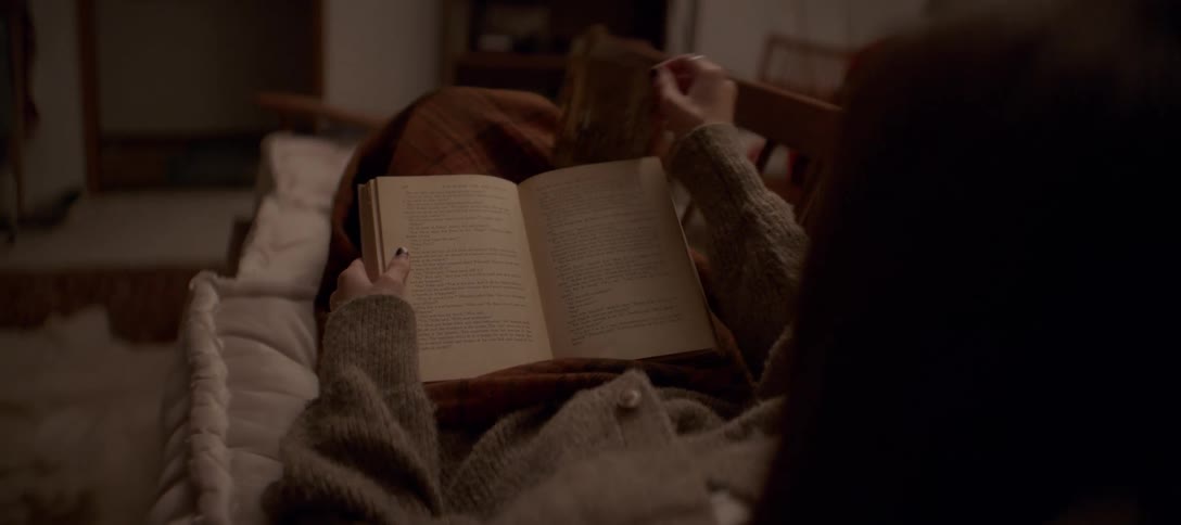 A woman cozies up with a blanket to read a vintage book and finds an old photograph inside