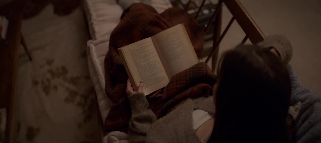 Overhead view of a cozy woman relaxing in a comfortable chair, wrapped in a plaid blanket and reading a book