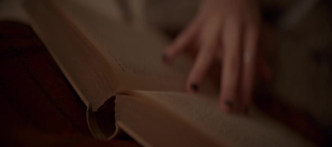 A soft-focus, intimate shot of a reader's hand turning the pages of an old book in warm, low light