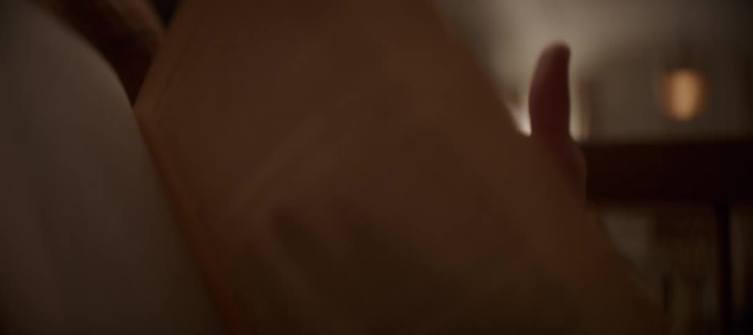 In a warm and cozy room, a person's hand gently turns the page of an old book
