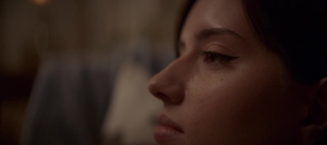 A close-up profile shot of a young woman as a single tear rolls down her cheek in a dimly lit room