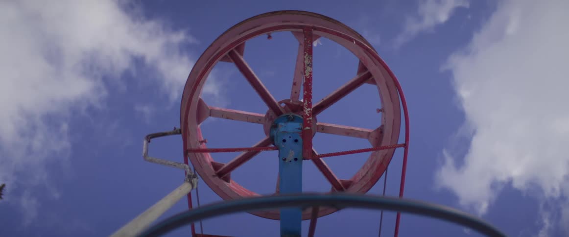 A point-of-view shot riding a T-bar ski lift shows the mechanical pulley wheel turning against a cloudy blue sky