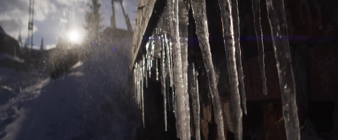 Sunlight glistens on melting icicles as they drip in slow motion on a cold winter day