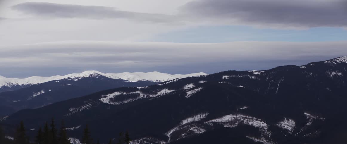 A stunning, wide view of a snowy mountain range under a vast, cloudy winter sky