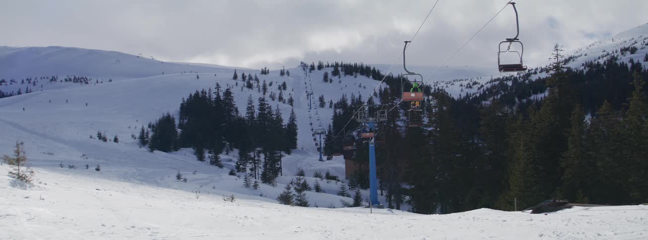 A long chairlift carries skiers up a snowy mountain slope at a ski resort on a cold, cloudy day