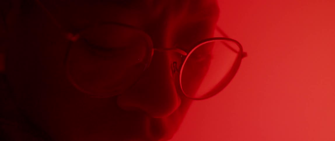 Person wearing glasses sits in a red lit room