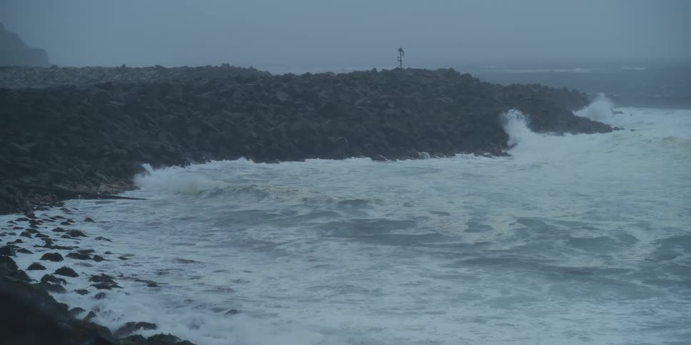 Slow motion shot of powerful ocean waves crashing against a rocky breakwater during a storm