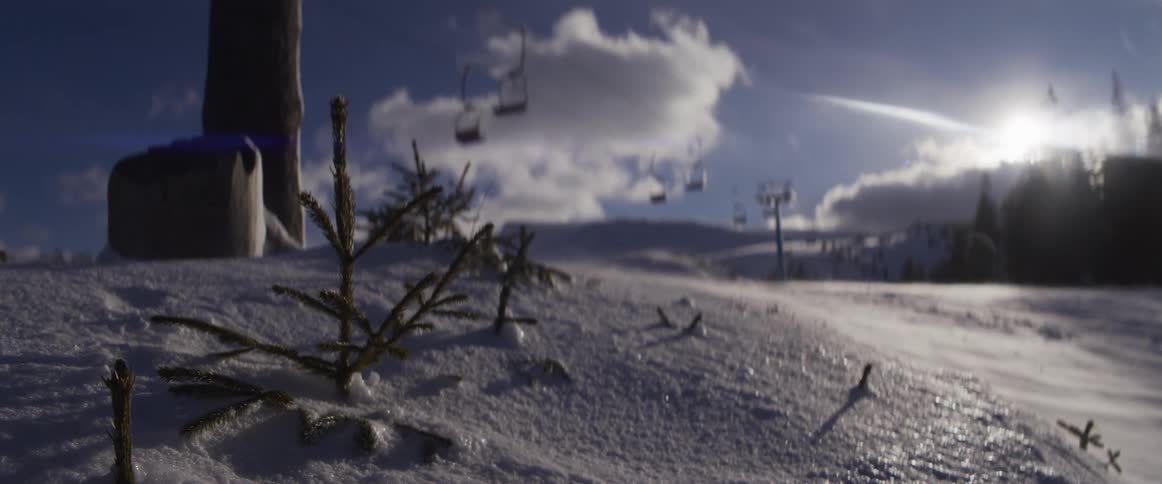 A small pine sapling stands in the foreground as wind blows snow across a ski slope with a chairlift in the background