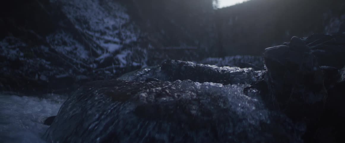 Dark, cold water cascades over rocks in a moody, slow-motion shot during winter