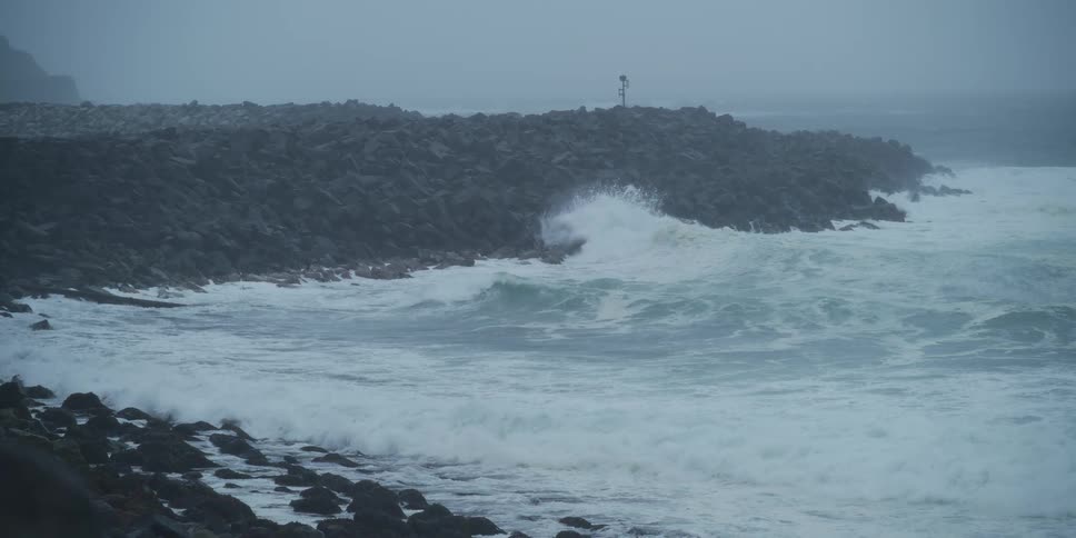 A slow-motion view of a tempestuous sea shows large waves breaking against a stone jetty during a storm