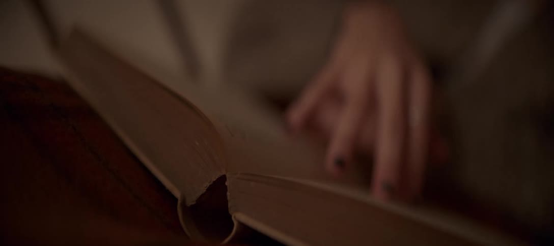 A person's hand slowly turns the pages of a well-loved book in a softly lit, cozy room