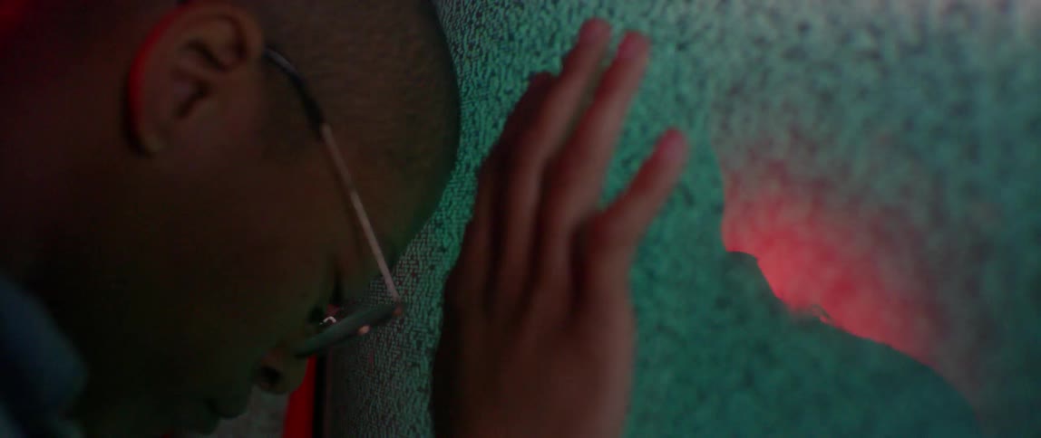 A person leans against a television screen playing static
