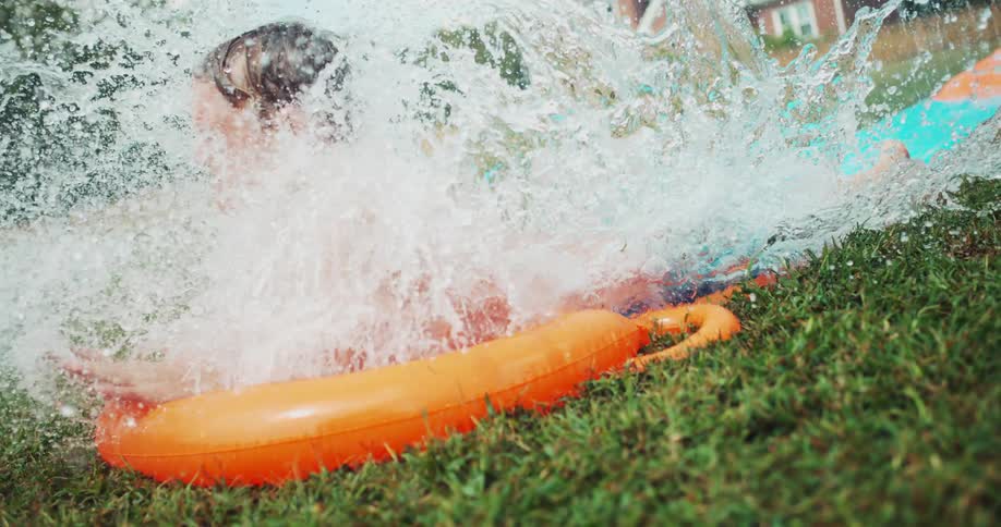 A child slides on a water slide splashing water everywhere