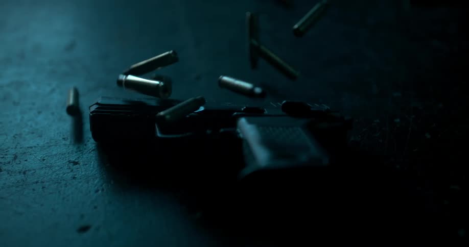A gun is on the ground in a dark room with bullets falling around it
