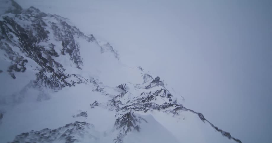 An exhilarating aerial flight follows a treacherous, snow-covered mountain ridge into the clouds