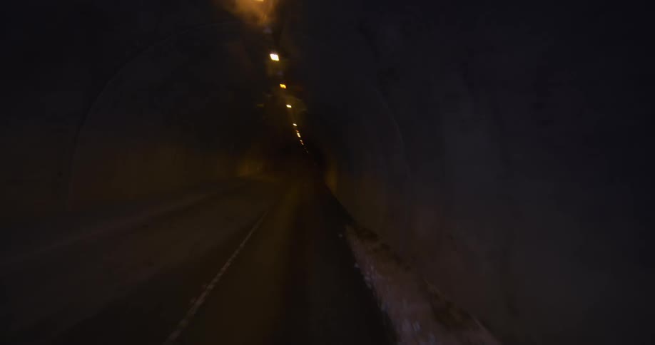 POV shot of a car driving out of a heavy snowstorm into a dark, dimly lit tunnel