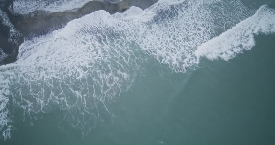 Mesmerizing aerial top-down view of gentle ocean waves crashing onto a snowy coastline