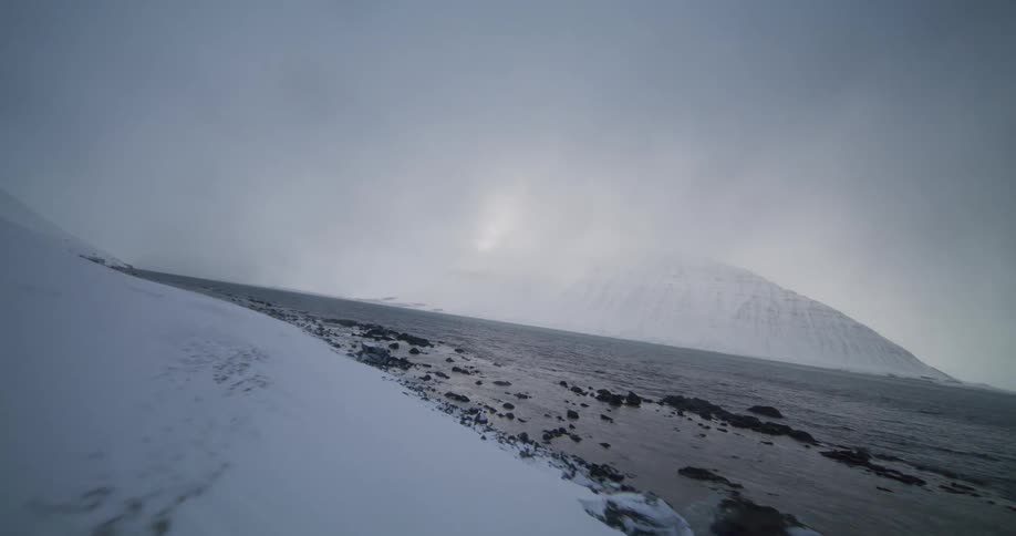 A slow drone flight reveals a vast, snow-covered fjord landscape on a cold and foggy day in Iceland