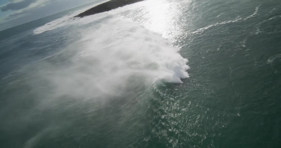A dramatic, slow-motion aerial view captures a lone surfer paddling alongside a colossal ocean wave as it breaks with immense power