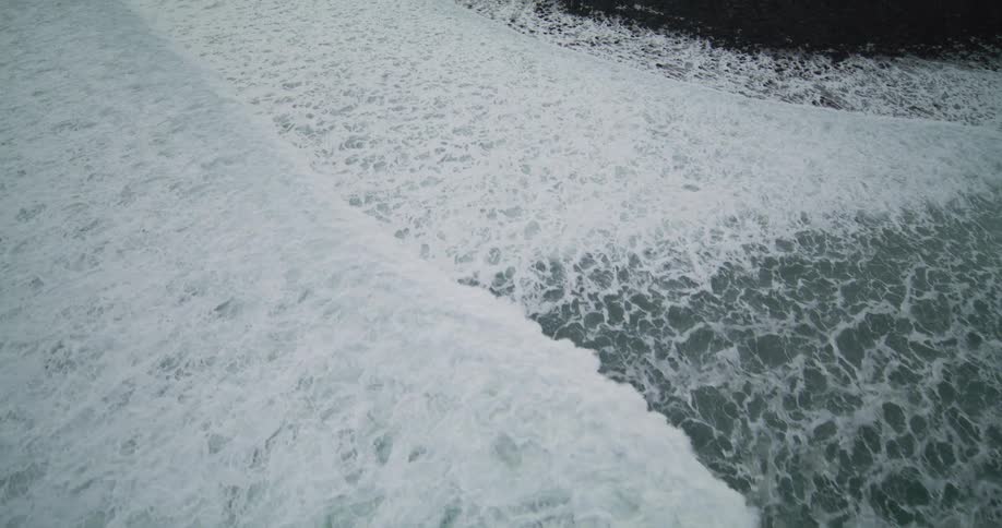 A mesmerizing aerial view of powerful ocean waves creating white foam as they roll towards the shore in slow motion