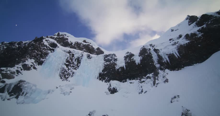 An exhilarating aerial flight ascends a majestic, snow-covered mountain with frozen waterfalls and icy cliffs