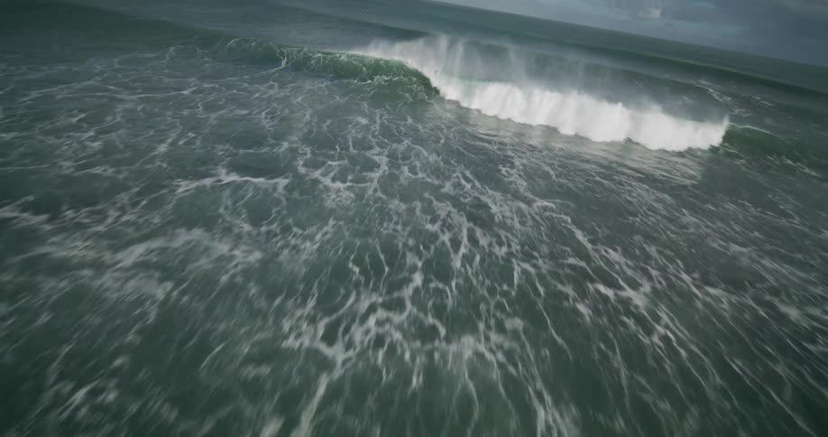 A dramatic slow-motion aerial follows a powerful ocean wave as it crashes, creating a misty spray with a faint rainbow
