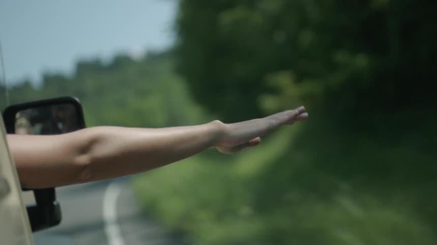 A person in a car is hanging their hand out of the window as it rides