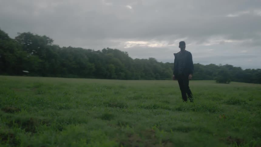 Man looking around in a grassy field on a cloudy day