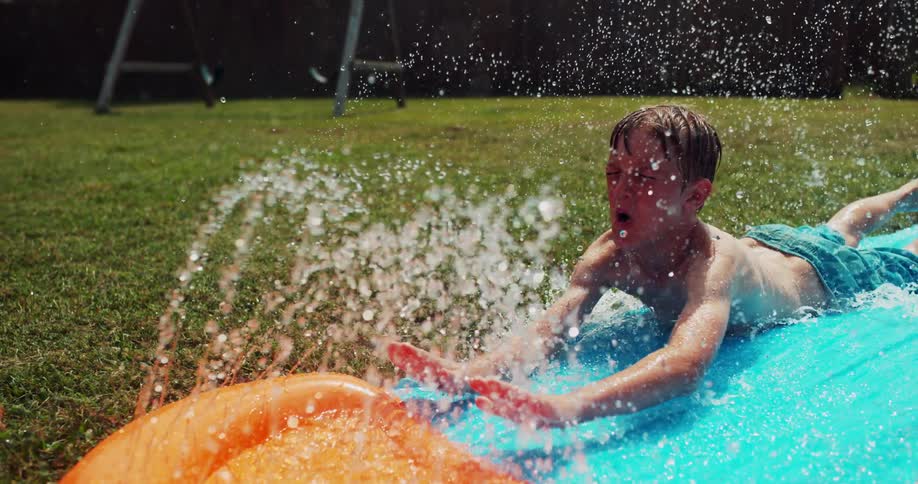 A boy slides down a slip 'n slide with water spraying all around