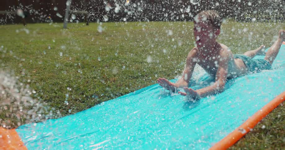 A boy slides on a waterslide in the yard