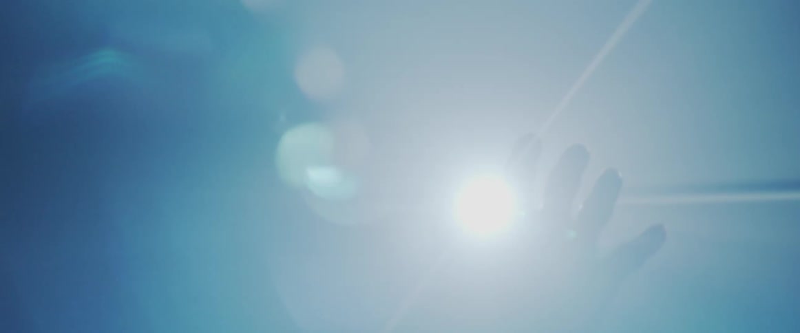 A person's hand partially blocks a bright light, while the light beams glimmer through the fingers