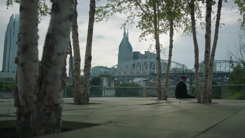 A man is sitting on the ground by the water before a city