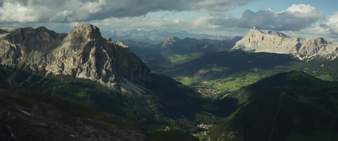A sweeping view of a majestic mountain range overlooking a sunlit valley and small town