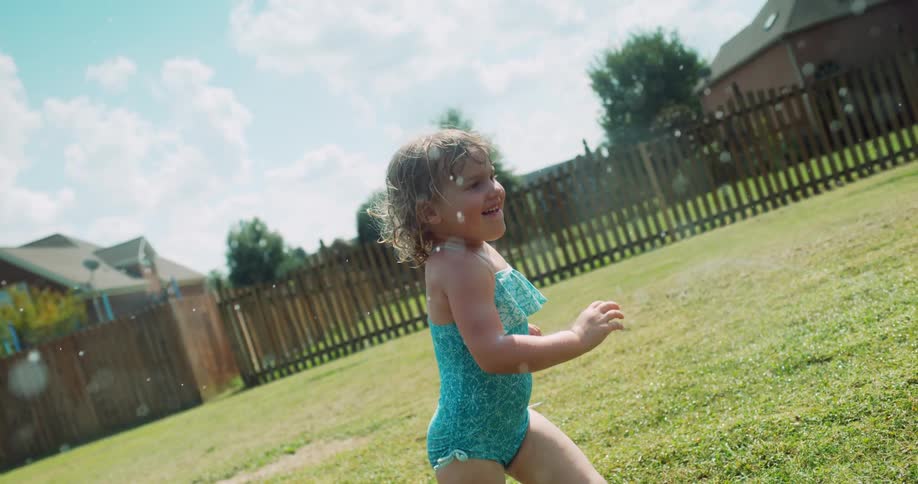 Little girl in a bathing suit runs through the sprinkler