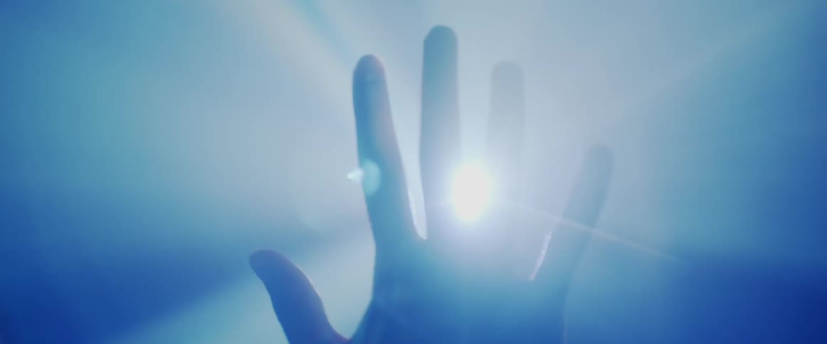 A hand being raised in front of a bright light spreads its fingers