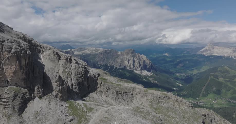 A stunning static aerial view of the majestic Dolomite mountain range overlooking a lush green valley under a dramatic cloudy sky